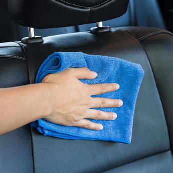 A hand using a blue microfiber cloth for car & bike on a car seat for effective cleaning
